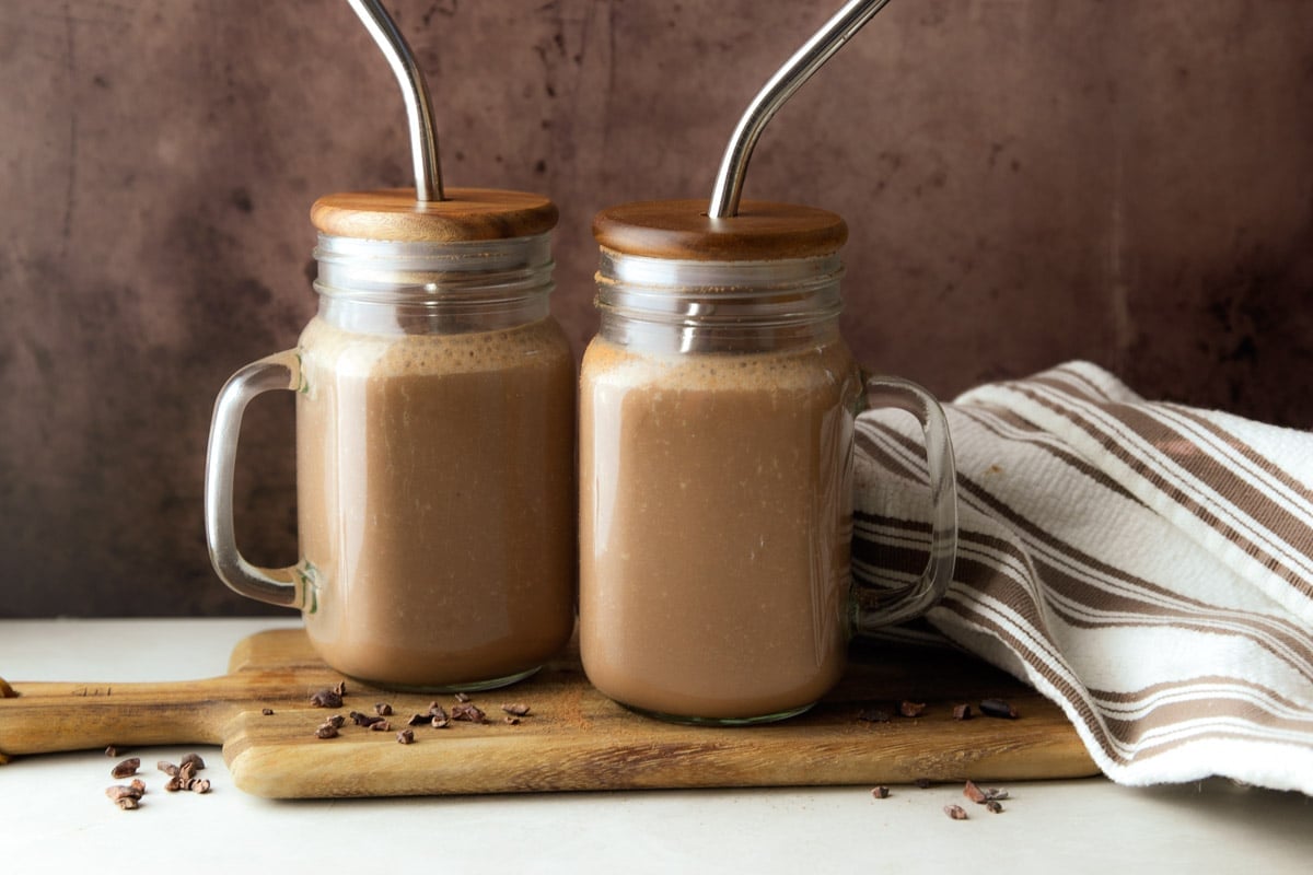 Chocolate Coffee Protein Smoothie in a glass jar on a wooden cutting board, and a white and brown dish towel. 