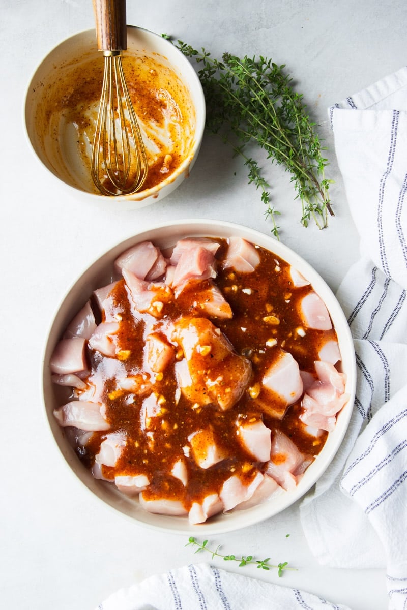 Cubed chicken covered in honey mustard sauce, fresh thyme, and a white and black dish towel. 