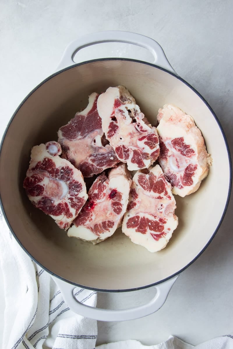 Raw oxtail in a pot with a white and black dish towel.