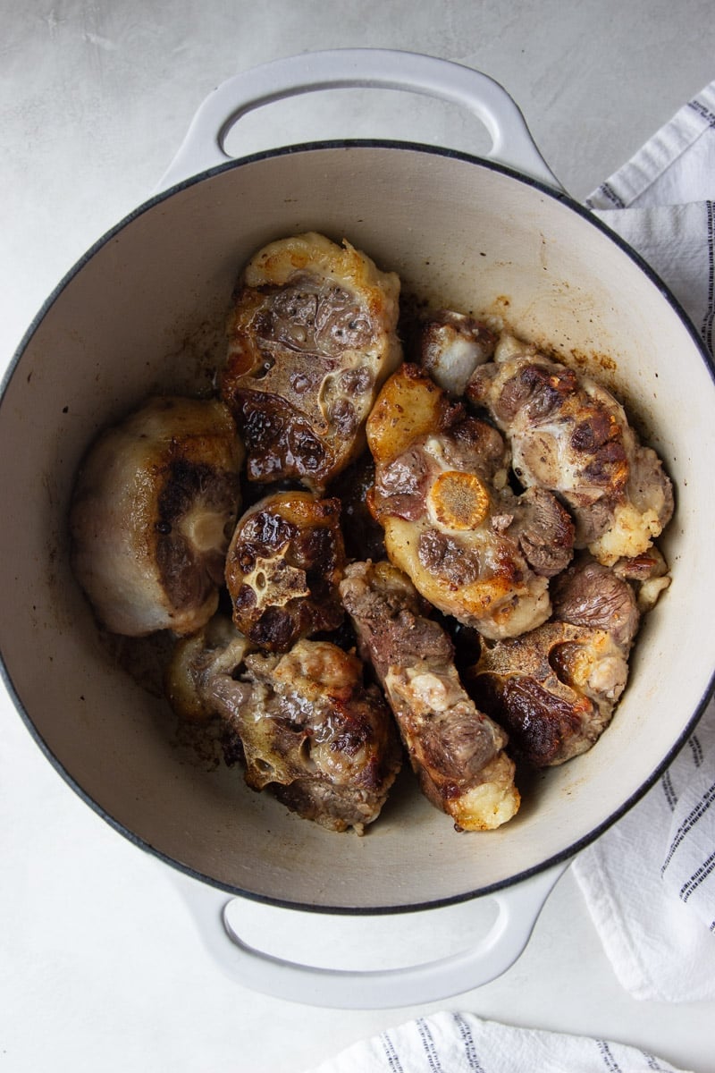 Seared oxtail in a pot with white and black dish towel. 