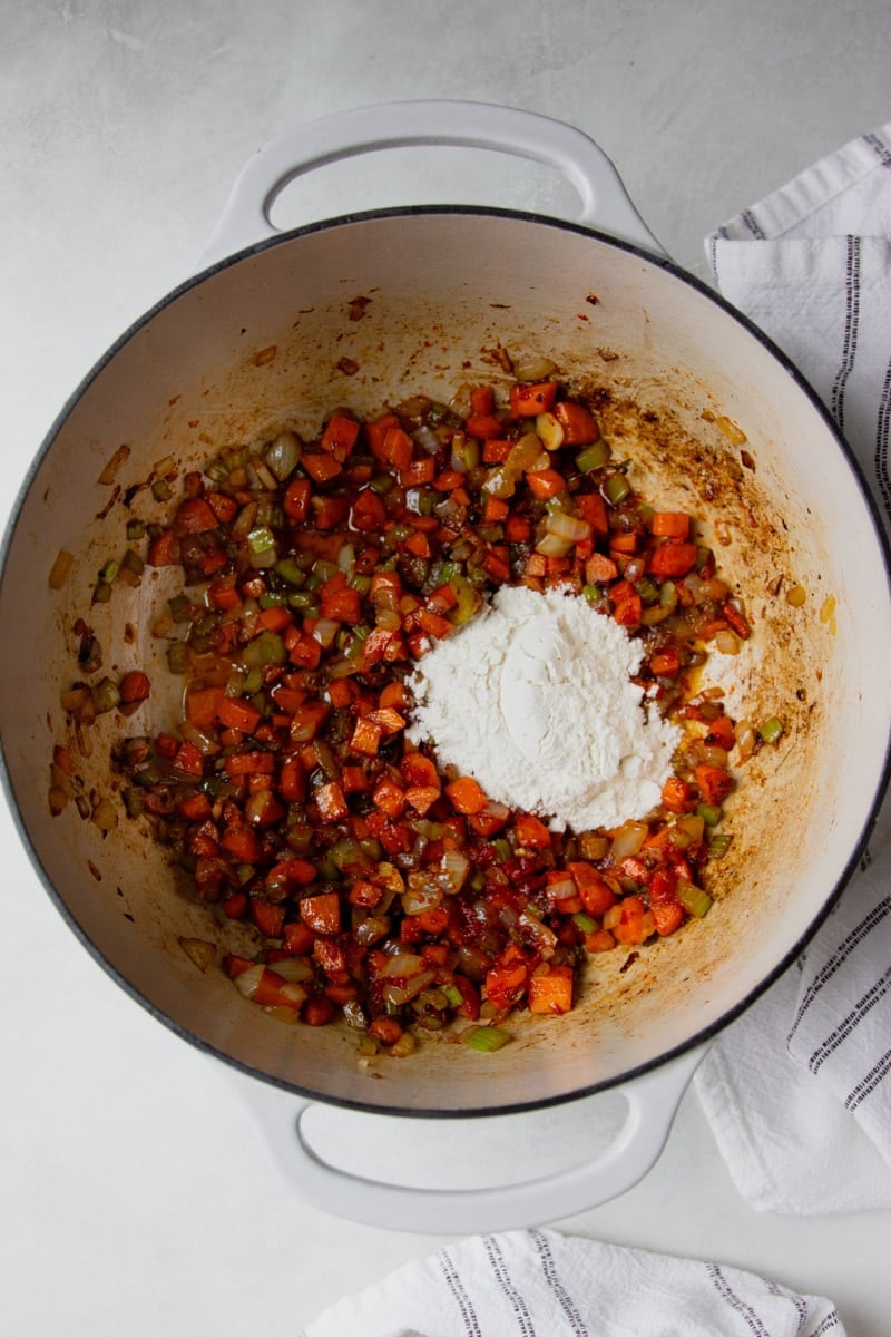 Sauteed veggies in a pot with flour and a white and black dish towel.