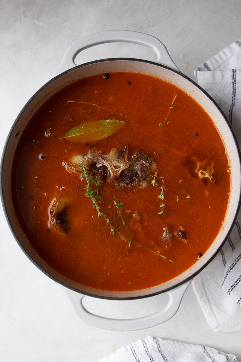 Oxtail soup in a white pot with a white and black dish towel.