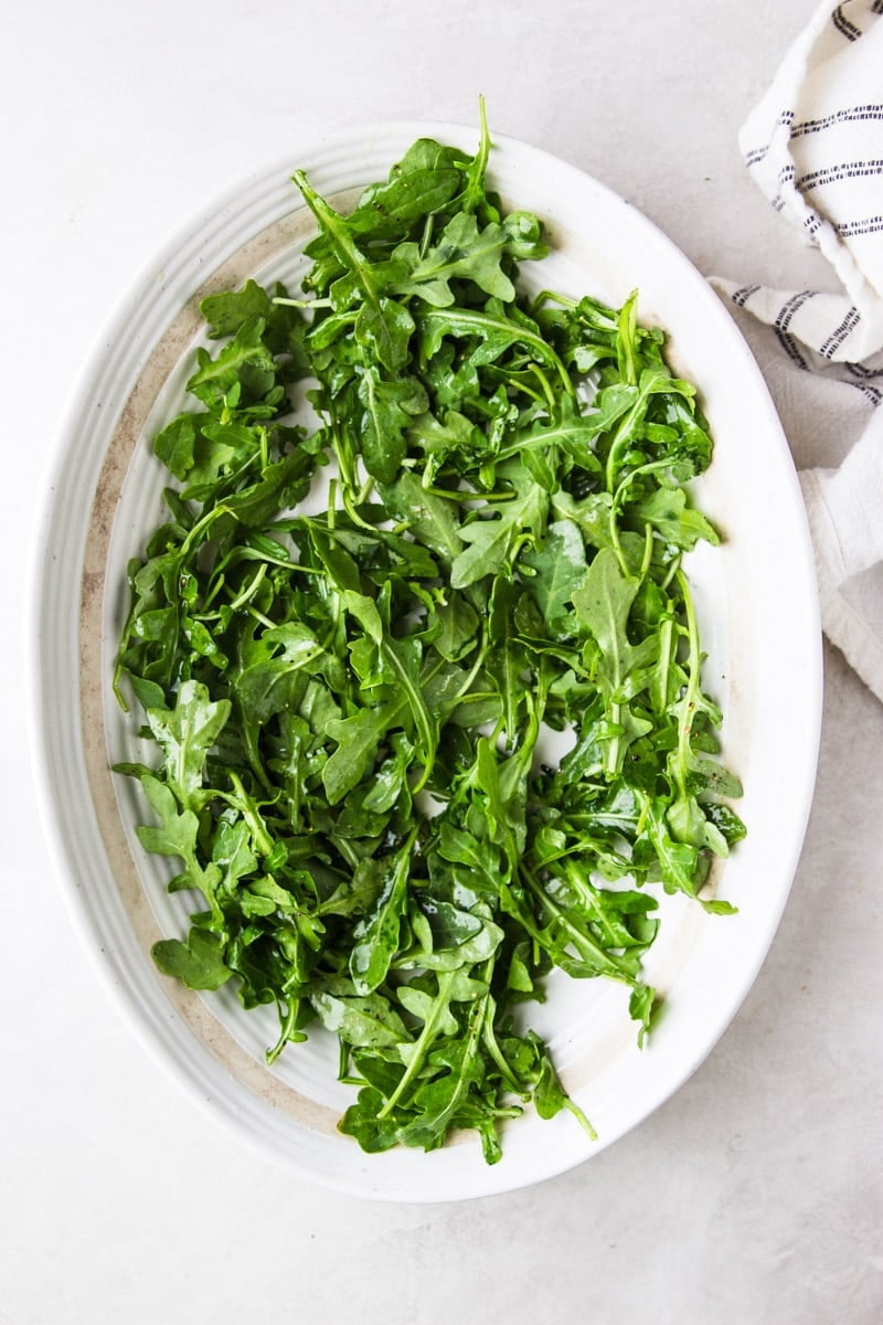 Arugula with pre-dressing on a white platter, white and black dish towel. 