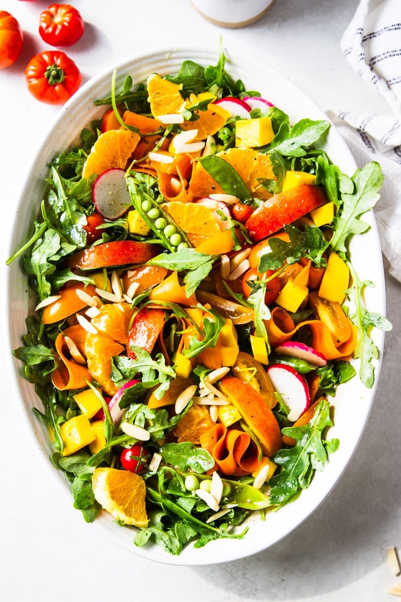 Arugula citrus salad on a white platter, tomatoes, white and black dish towel.