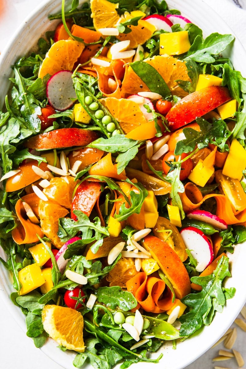 Arugula citrus salad on a white serving platter, almond slivers. 