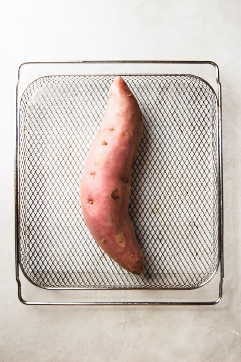 Unpeeled sweet potato in an air fryer basket. 