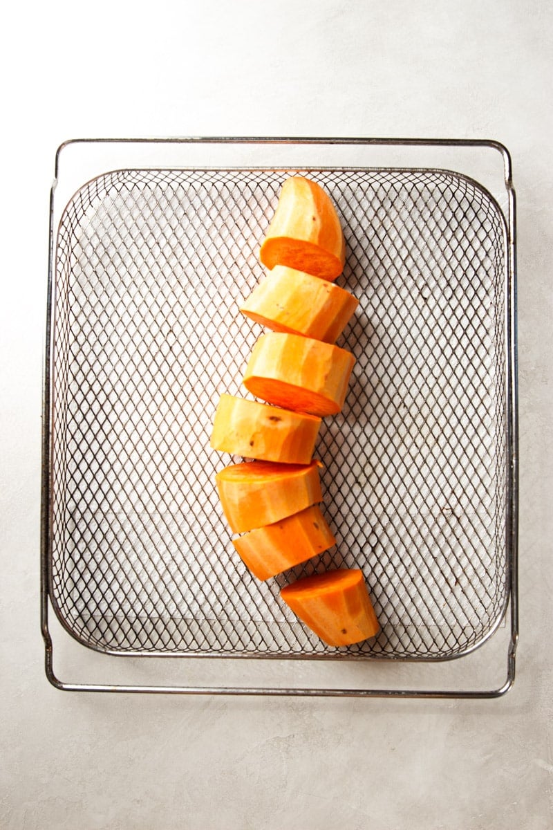 Peeled and chopped sweet potato in an air fryer basket. 