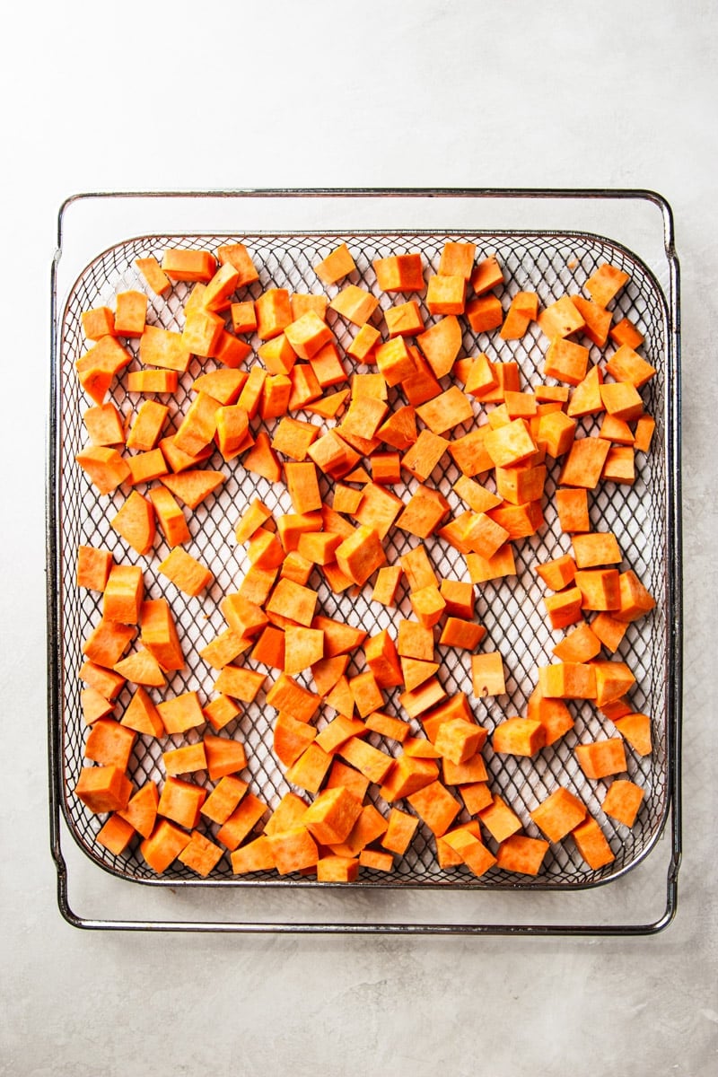 Peeled and cubed sweet potato in an air fryer basket. 