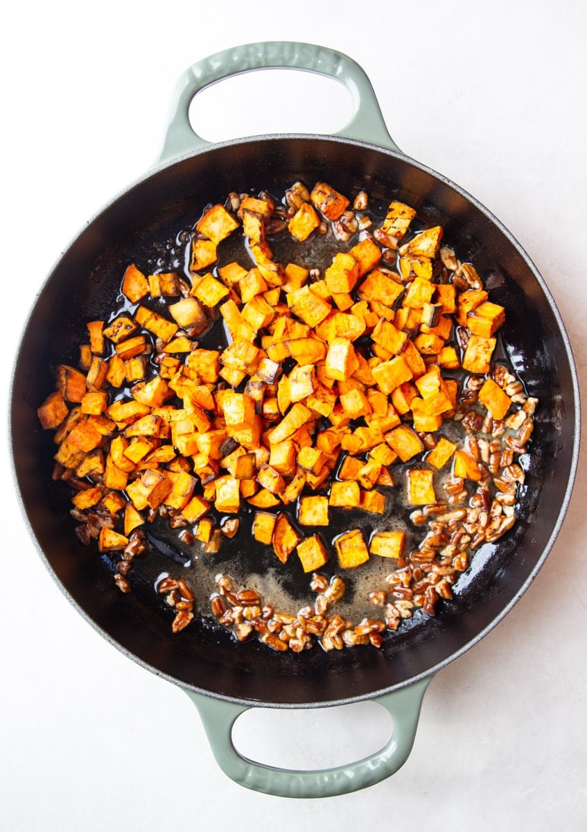 Cooked sweet potato in a skillet with pecans and maple butter. 