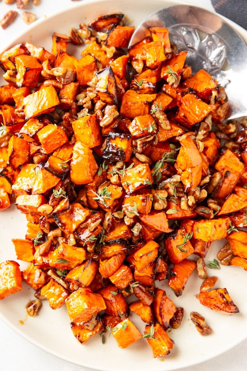 Cooked maple sweet potatoes with pecans and fresh thyme, silver spoon, plaid cloth. 