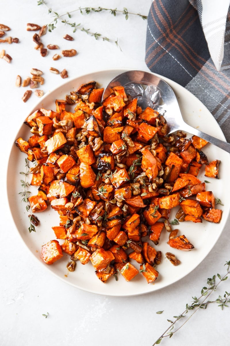 Cooked maple sweet potatoes with pecans and fresh thyme, silver spoon, plaid cloth. 