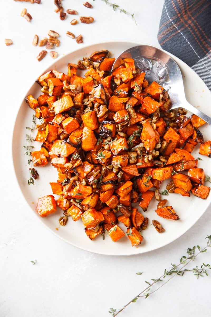 Maple sweet potatoes, pecans, silver spoon, white plate, fresh thyme, and plaid cloth.