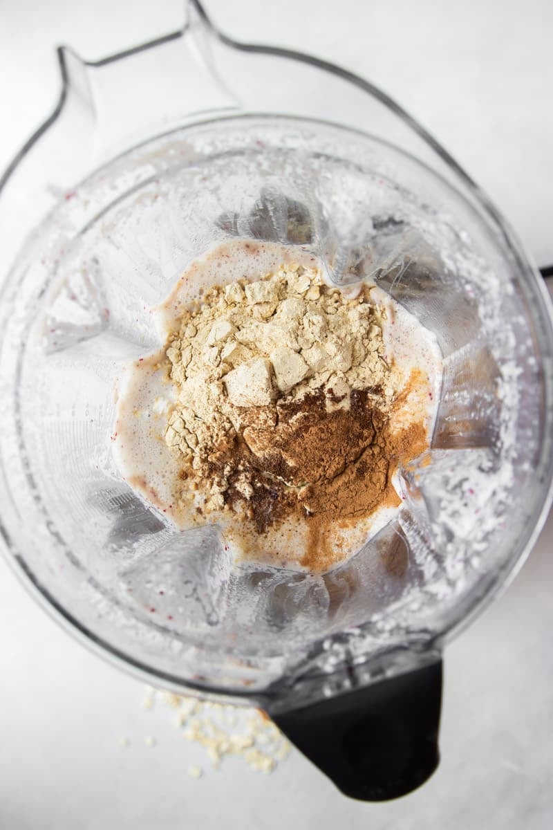 Cinnamon, cloves, protein powder with milk and yogurt in the bowl of a blender.