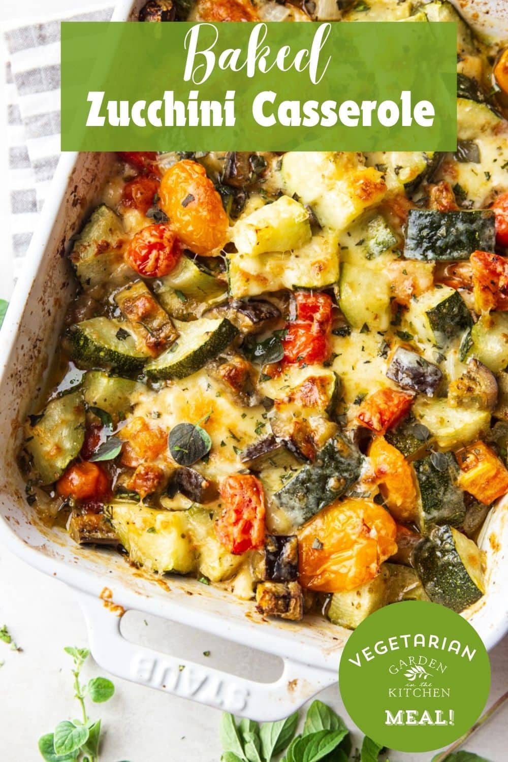 Baked zucchini casserole in a white baking dish, grey and white dish towel, and oregano. 