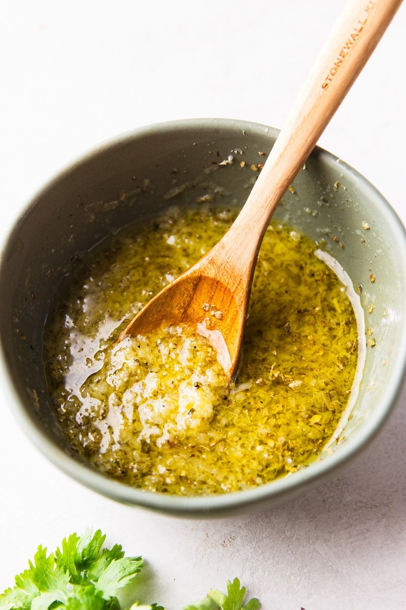 Seasoning mixture of olive oil, parmesan cheese, dried oregano in a bowl with a wooden spoon and cilantro. 