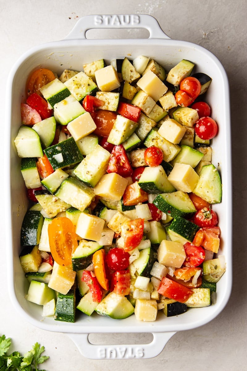 Chopped zucchini, eggplant, tomatoes, and onions with dressing in a white casserole dish, and cilantro.  