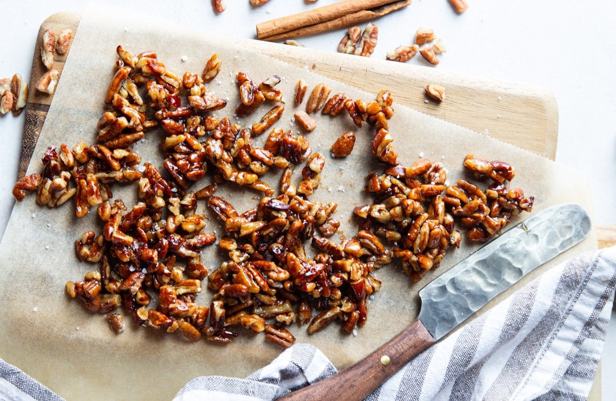 Maple coated pecans on a piece of parchment paper, knife, white and black dish towel.