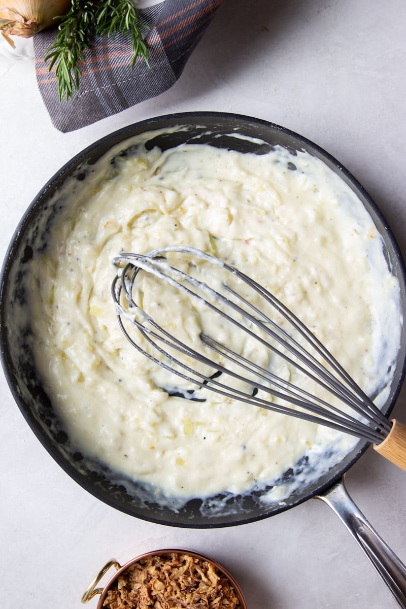 Adding flour to the aromatics and whisk to combine, onion, rosemary, and a plaid dish towel, crispy onions. 