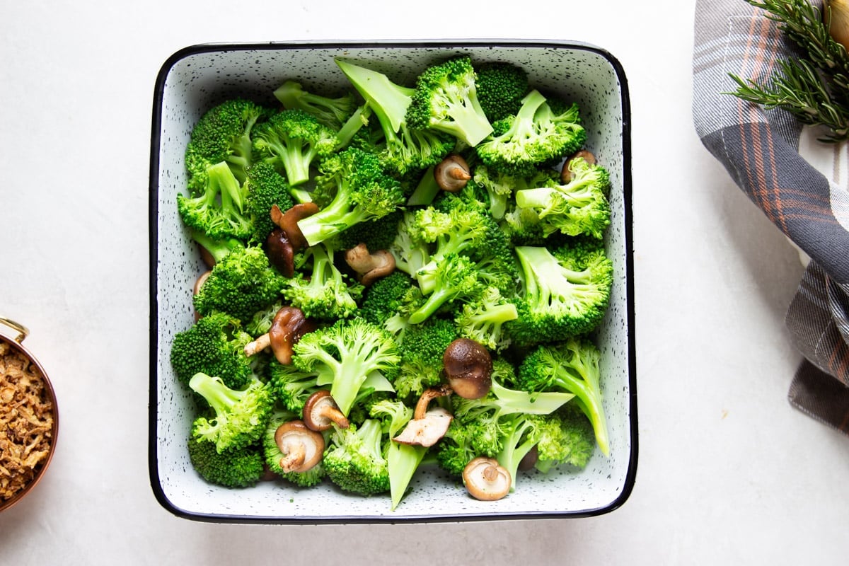 Broccoli and baby shiitake mushrooms in a casserole, crispy onions, plaid dish towel.