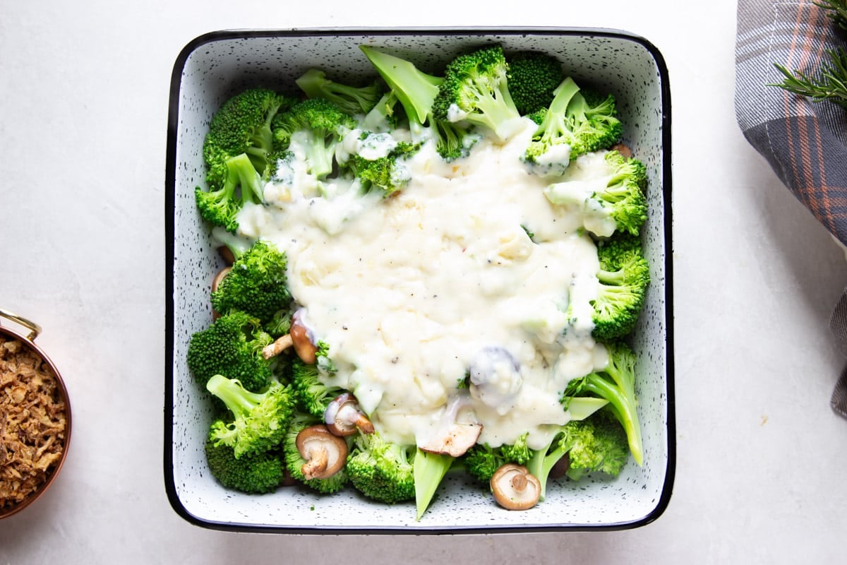 Broccoli and baby shiitake mushrooms with cream sauce poured over, crispy onions, and a plaid dish towel.