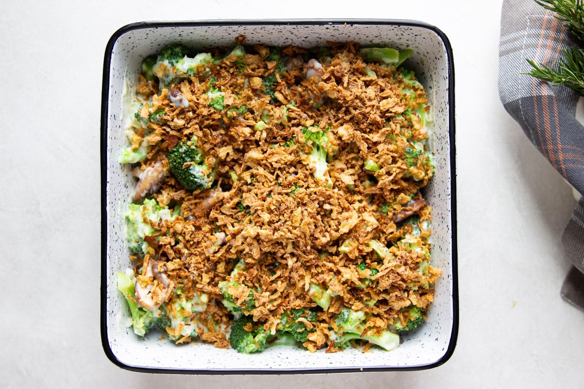 Broccoli and mushroom casserole with crispy onions, plaid dish towel, and rosemary.