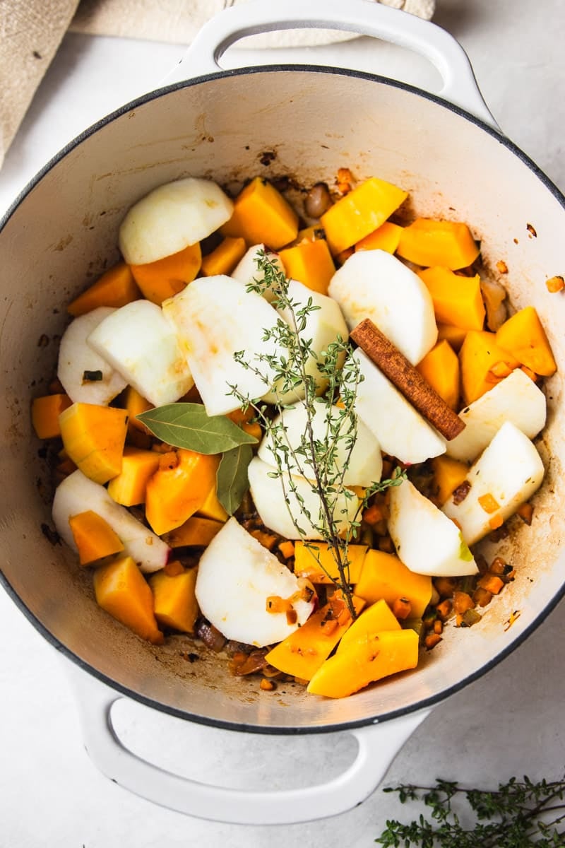 Apples, cinnamon stick, butternut squash and fresh thyme added to the pot, fresh thyme, and a dish towel. 