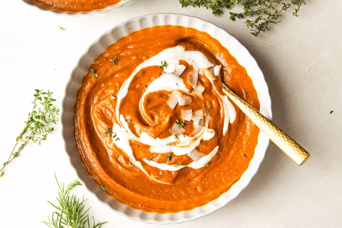 Butternut squash apple soup drizzled with yogurt and topped with coconut chips in white bowls and fresh thyme.