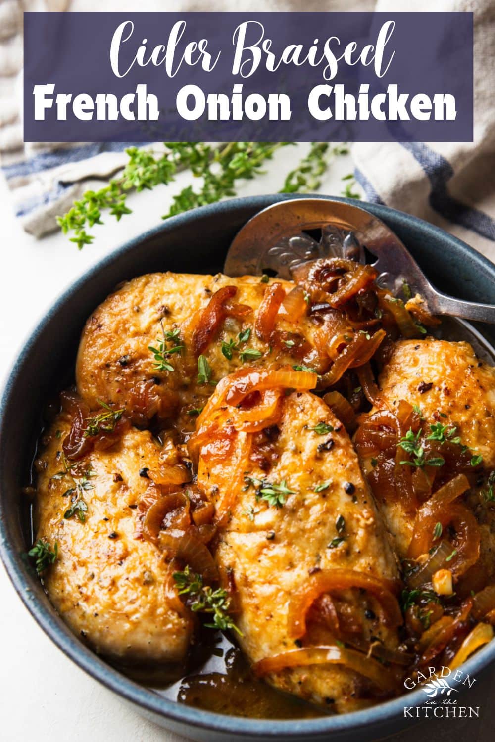 Cider braised chicken in a pot with a silver spoon, striped dish towel, and fresh thyme. 