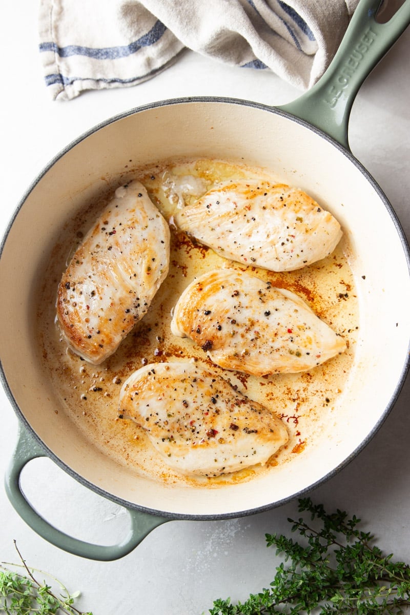 Seasoned chicken filets in a pot, fresh thyme, and a striped dish towel. 