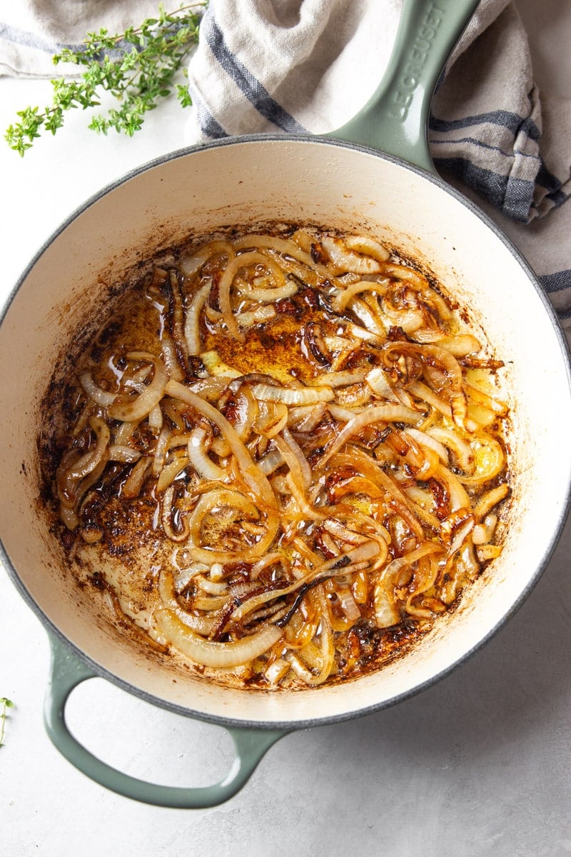 Caramelized onions in a pot, fresh thyme, and a striped dish towel. 