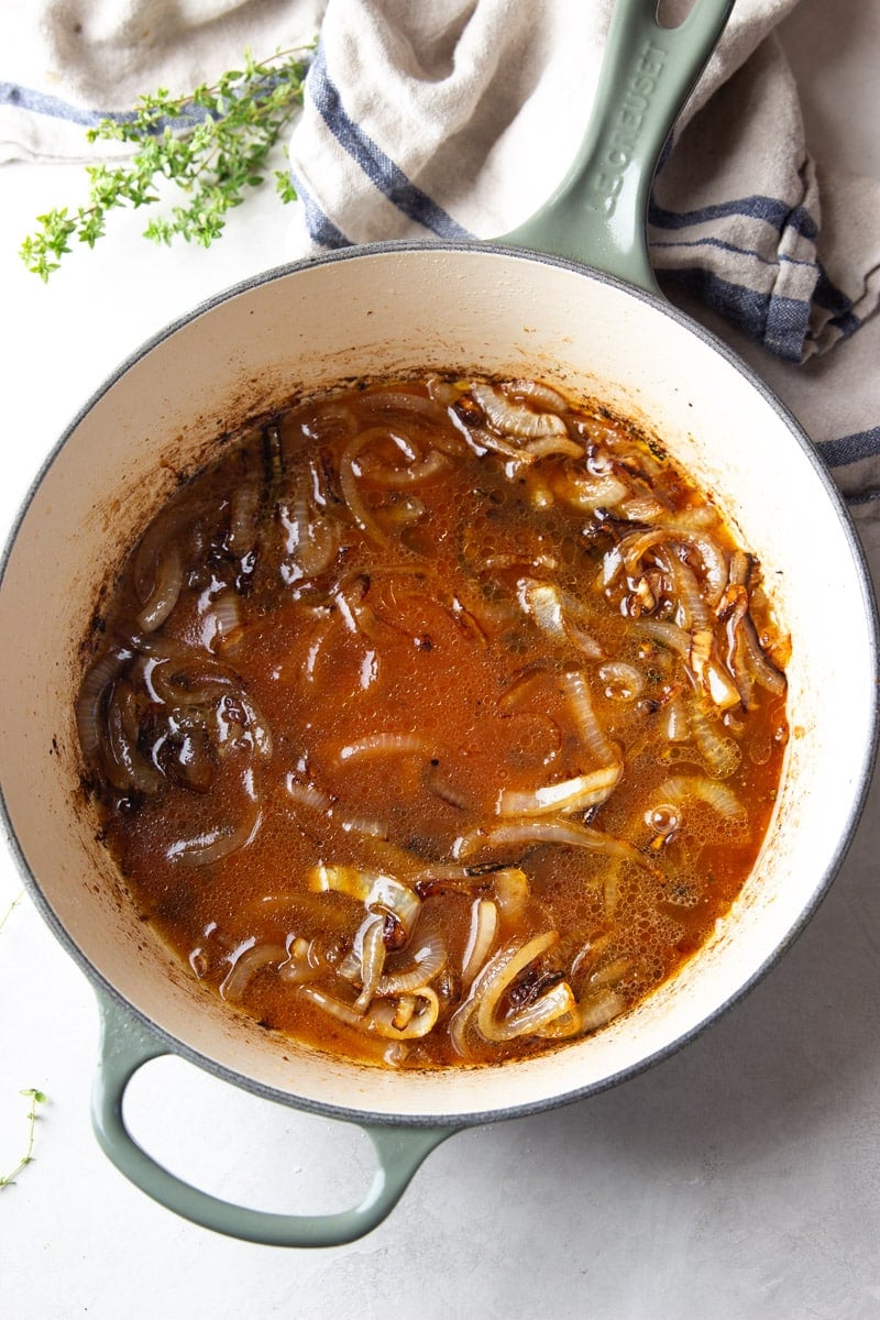 Caramelized onions in a pot with apple cider, fresh thyme and a striped dish towel. 