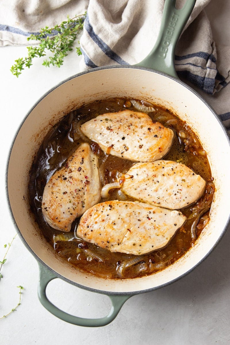 Chicken on top of the caramelized onions in a pot. fresh thyme and a striped dish towel. 