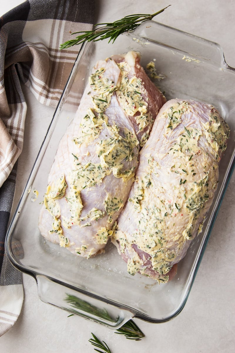 Turkey breasts covered in herb butter in a glass baking dish.