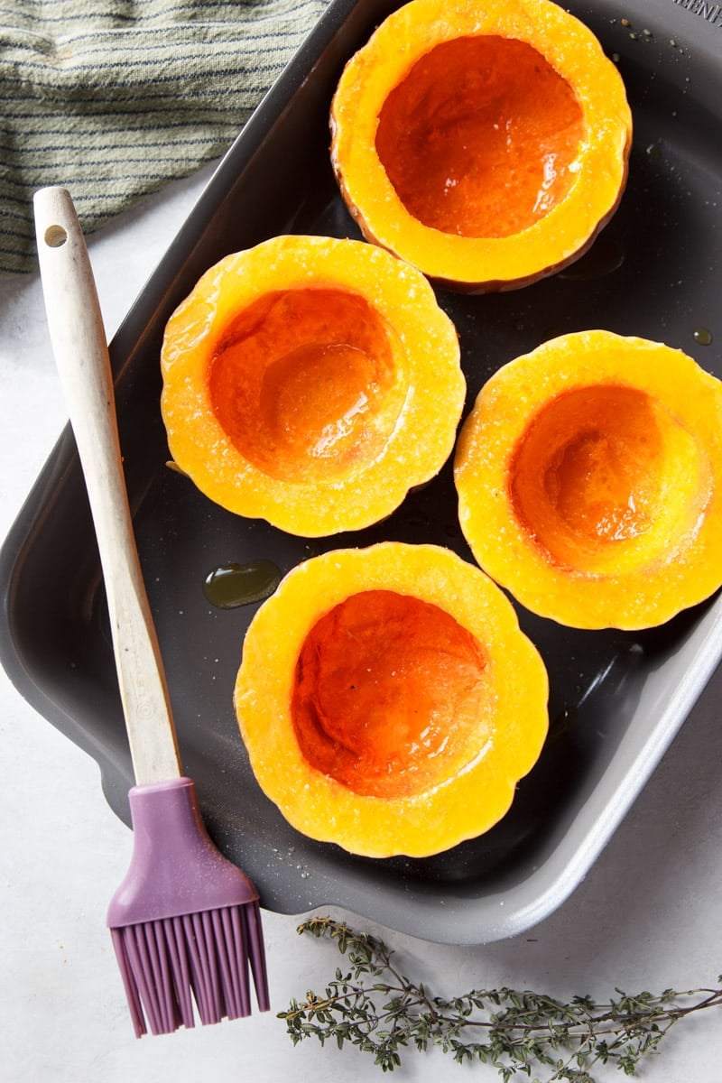 Koginut squash in a baking tray, a pastry brush, a striped dish towel and fresh thyme.