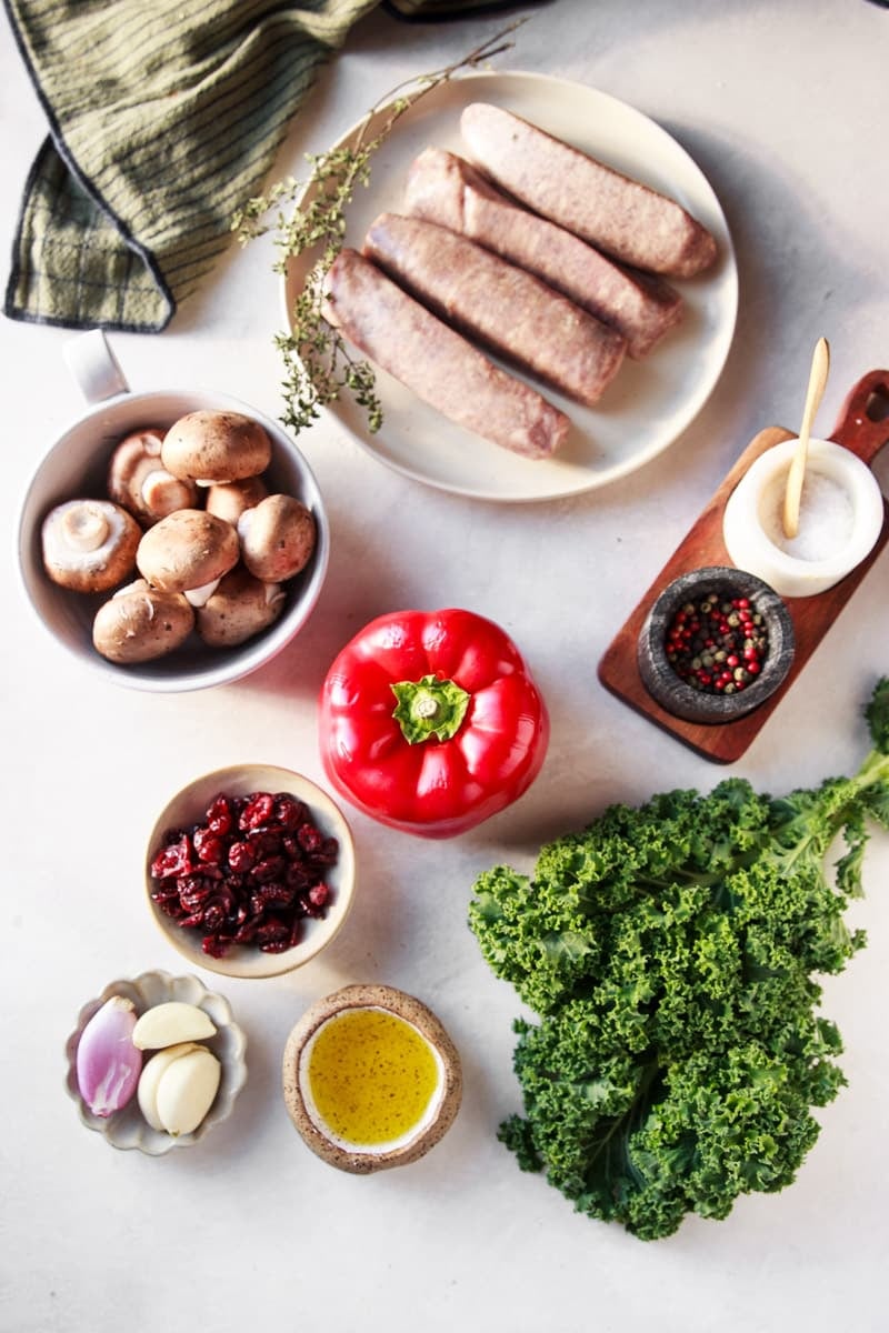 Sausage, baby bell mushrooms, bell  pepper, salt and pepper, striped dish towel, cranberries, garlic, shallot, and olive oil. 