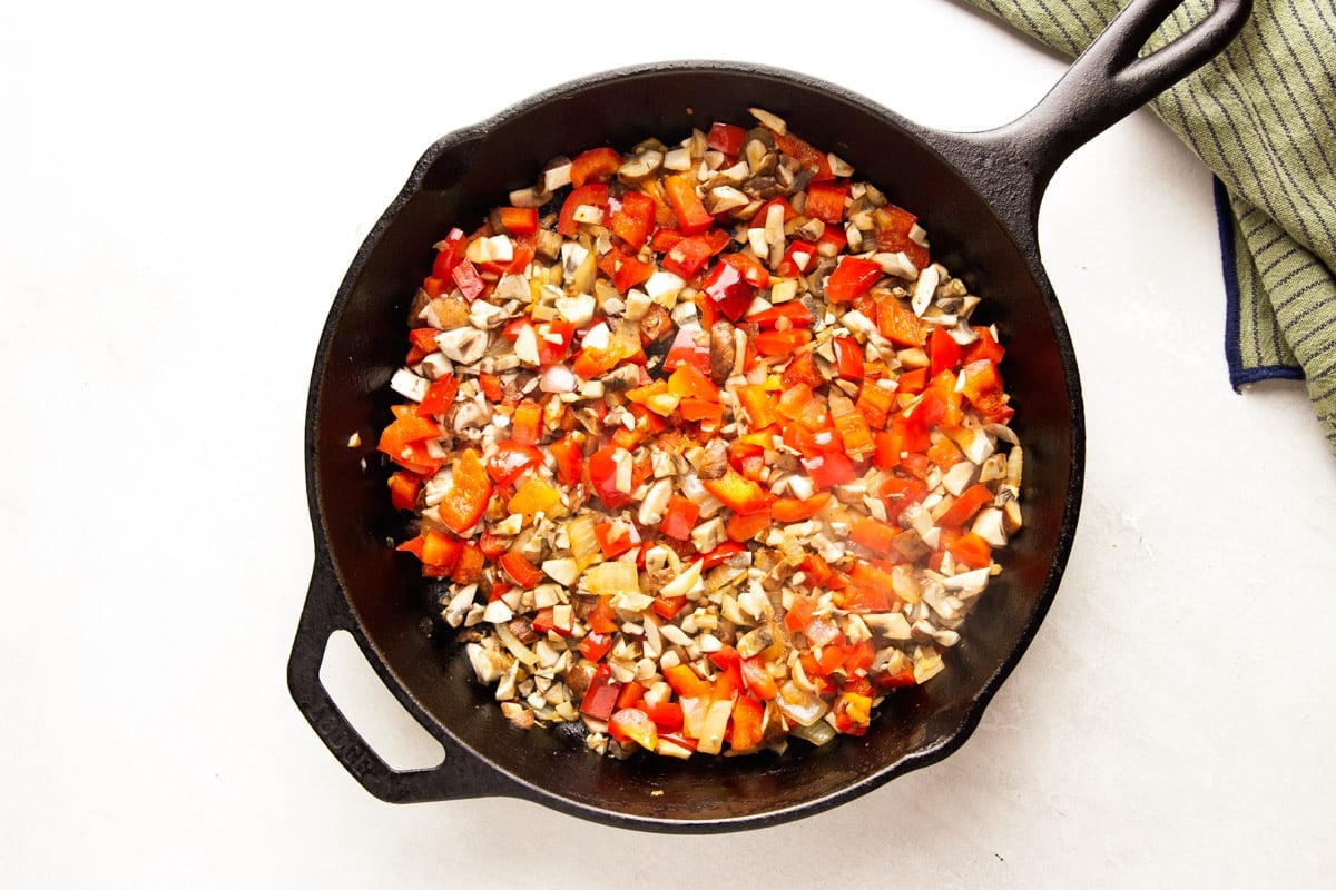 Chopped veggies in a cast iron pan, striped dish towel. 