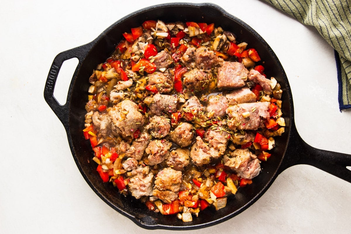 Chopped veggies with sausage in a cast iron pan, and a dish towel. 