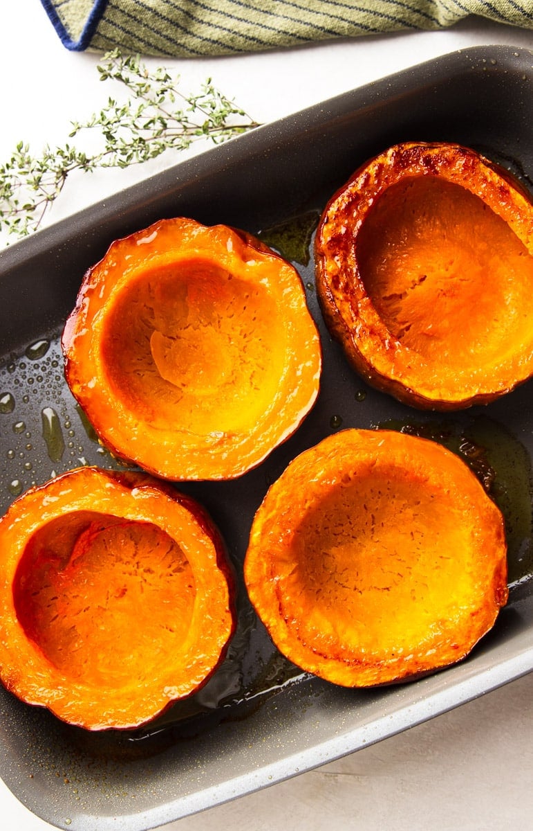 Roasted koginut squash in a baking tray, fresh thyme, and a striped dish towel. 