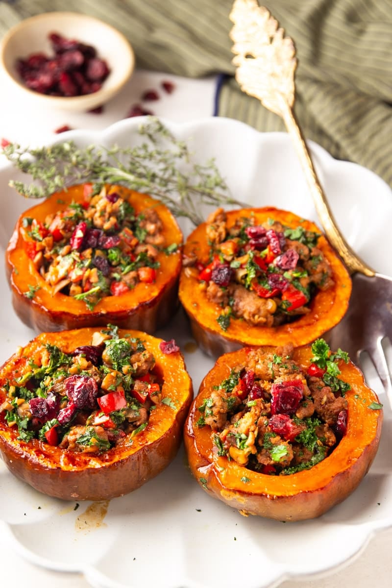 Sausage and kale stuffed koginut squash on a serving tray with a silver fork, cranberries and a striped dish towel. 