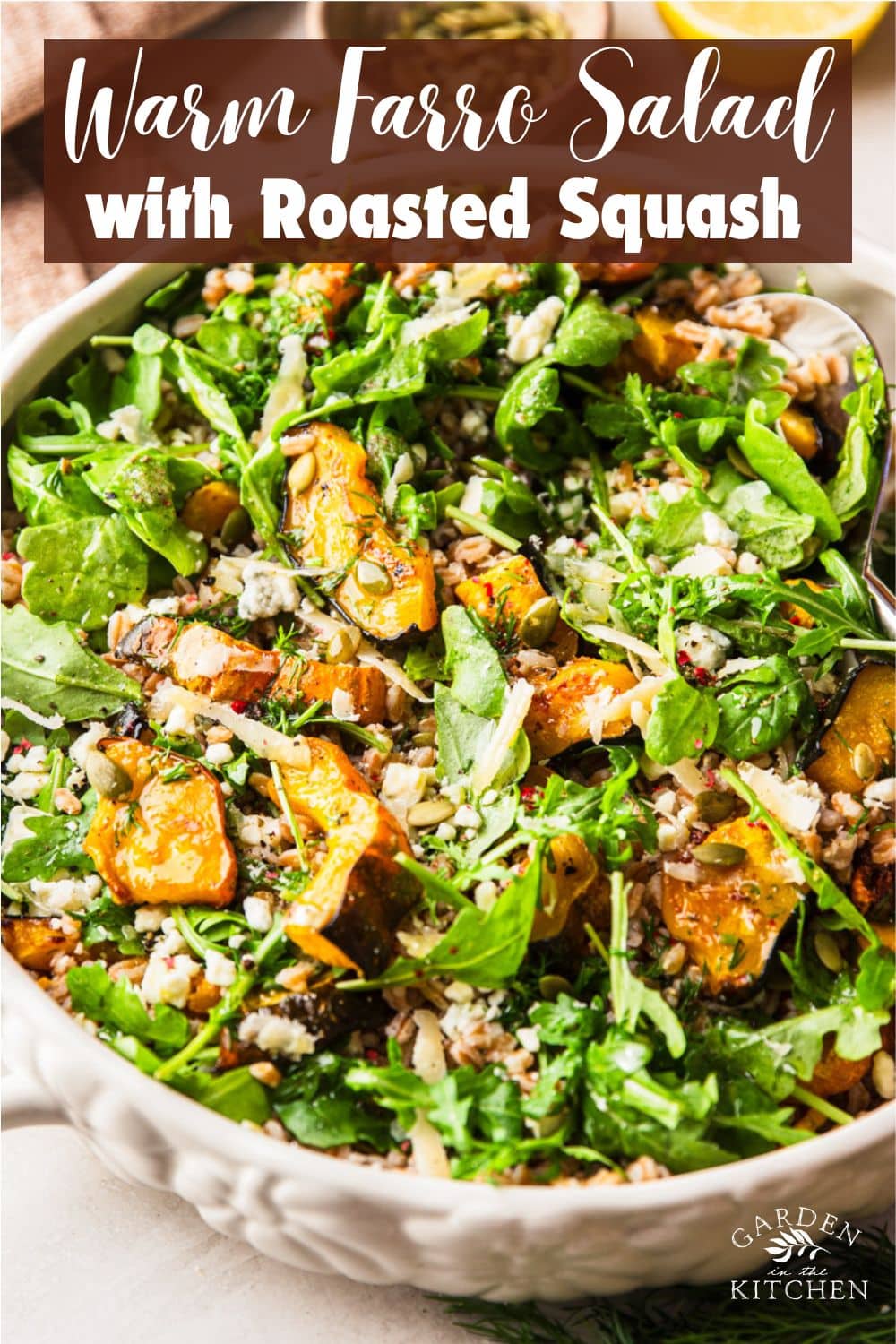 Warm farro salad with roasted squash in a bowl with a spoon, a bowl of pumpkin seeds, half a lemon, and fresh dill. 