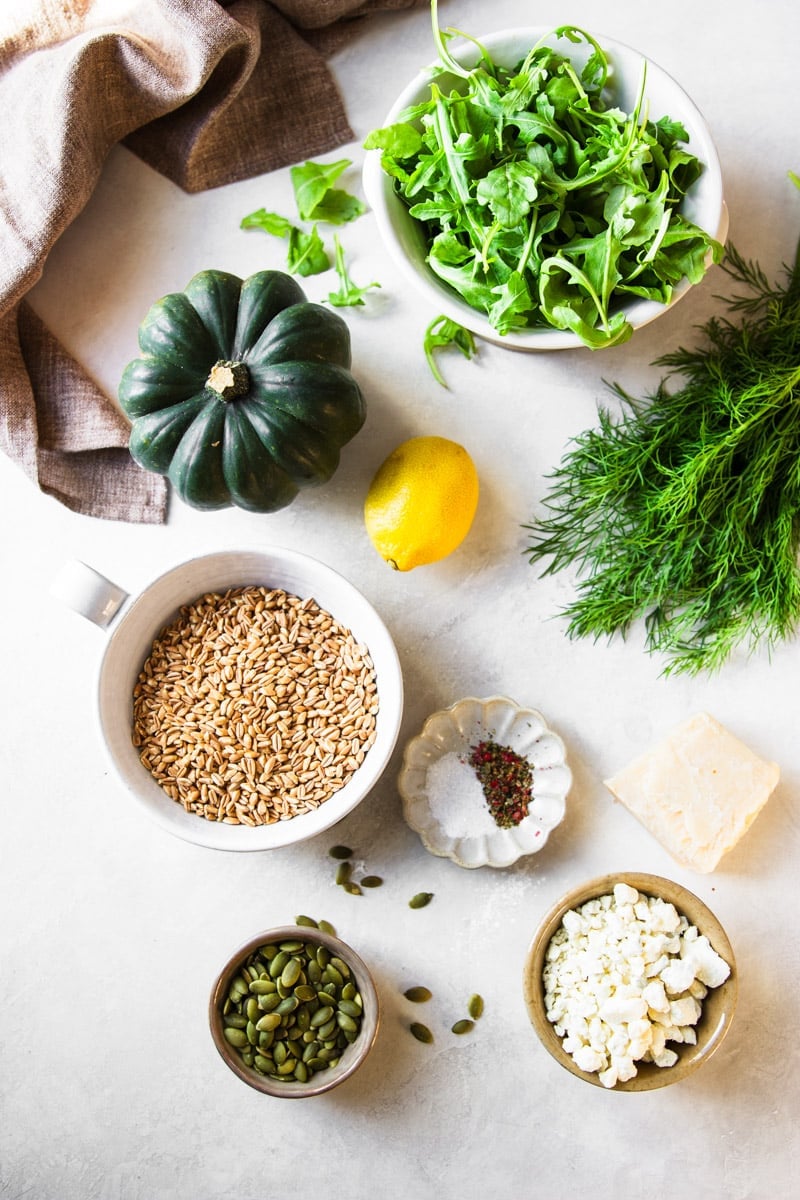 Acorn squash, bowl of arugula, fresh dill, a lemon, farro, salt and pepper, block of parmesan cheese, a bowl of crumbled blue cheese, and a bowl of pumpkin seeds. 