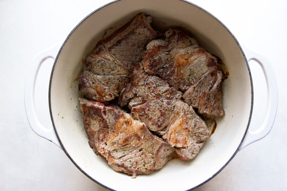 Browned beef in a white Dutch oven. 