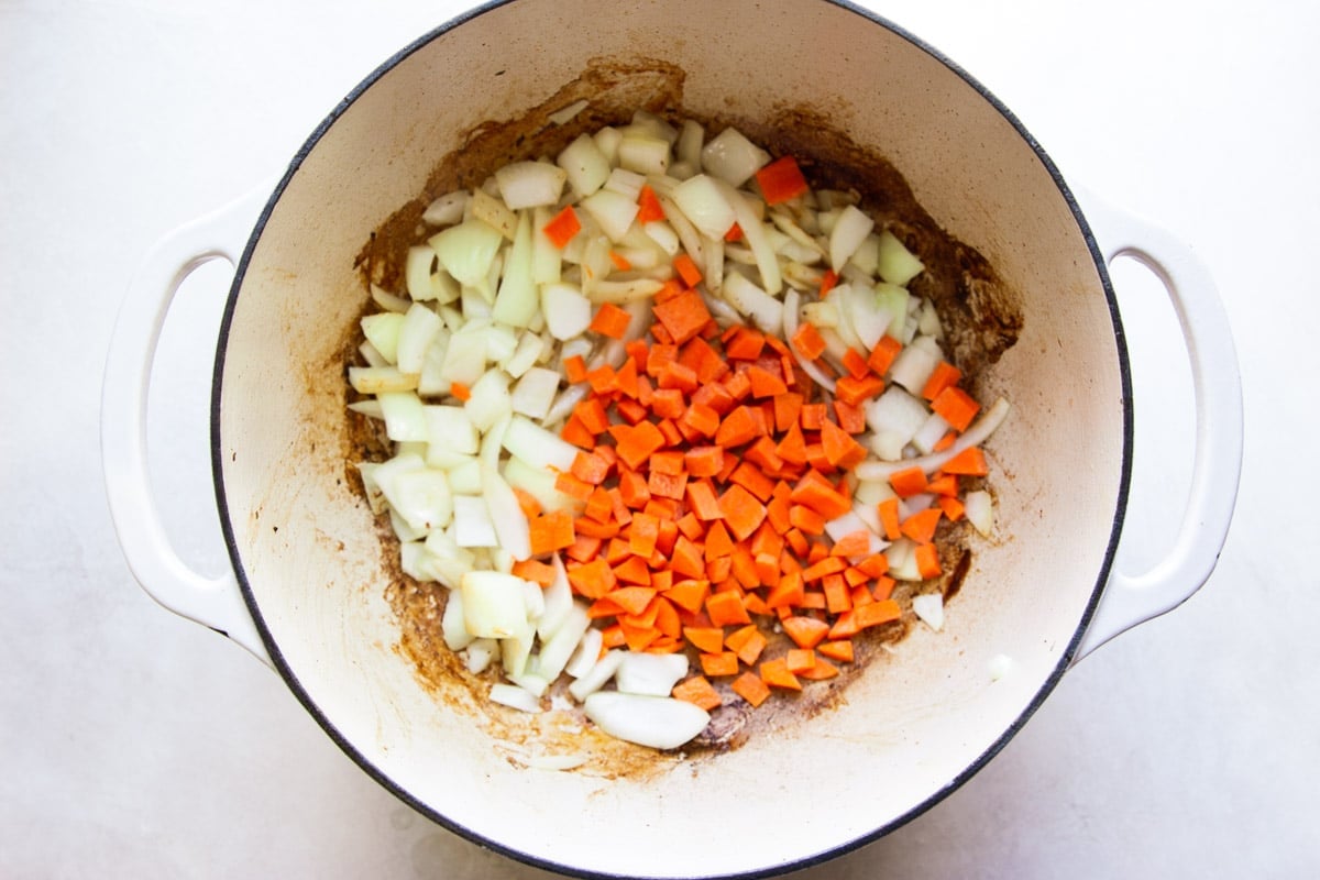 Chopped onions and diced carrots in a white Dutch oven. 